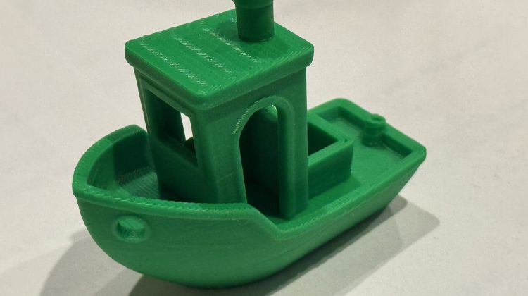 Standard "Benchy" 3D printed model in green PLA against a white background. Benchy is a small stylized cartoon-like boat.